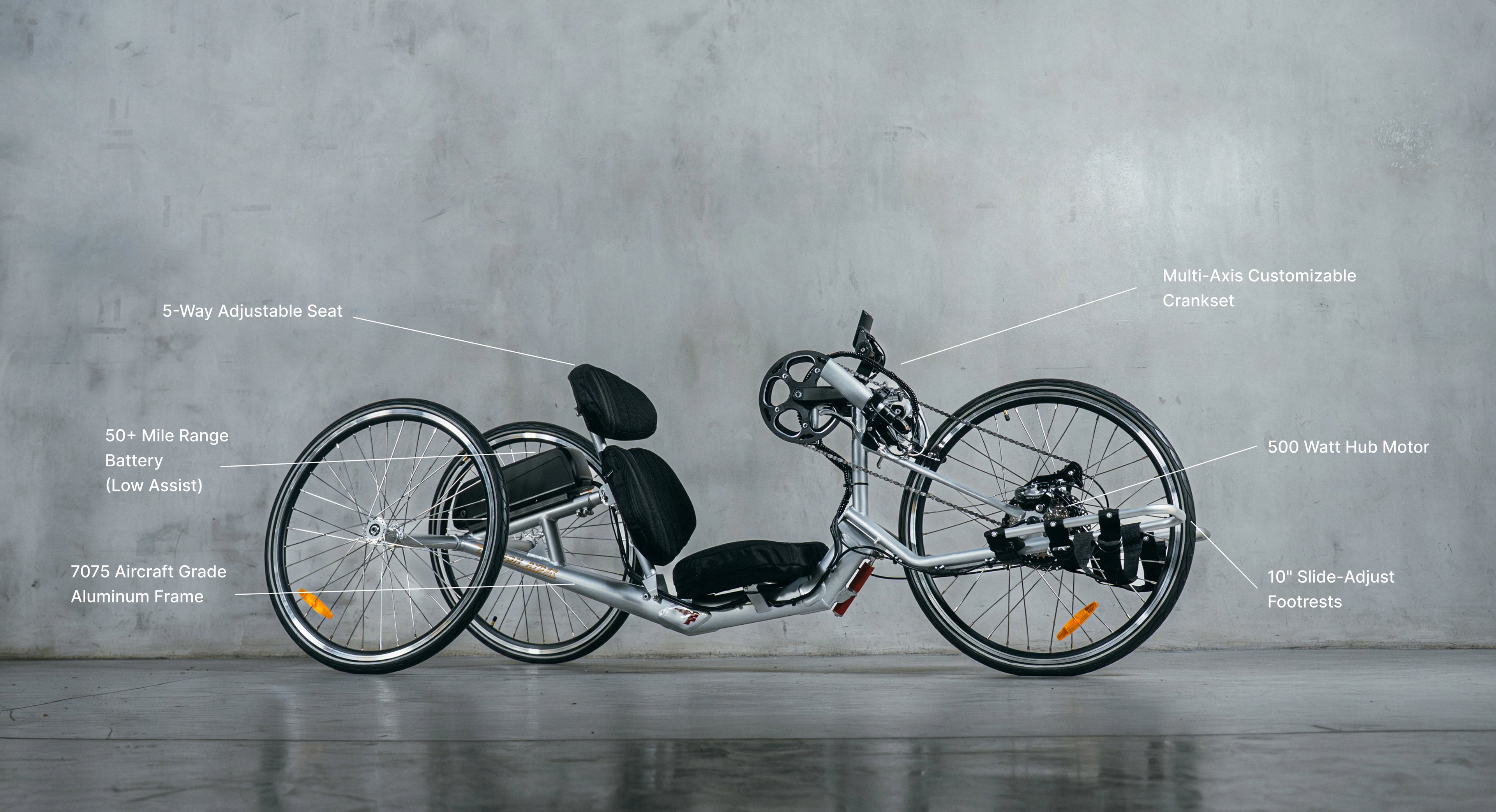A silver electric handcycle against a grey wall with text callouts highlighting its adjustable seat, 50-mile range battery, aircraft-grade frame, customizable crankset, hub motor, and adjustable footrests.